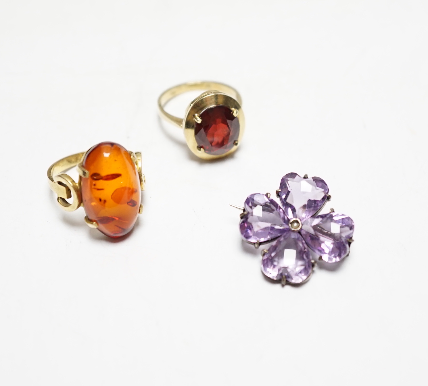 A 333 yellow metal and amber set ring, a 585 and gem set ring and an amethyst and seed pearl set white metal brooch.